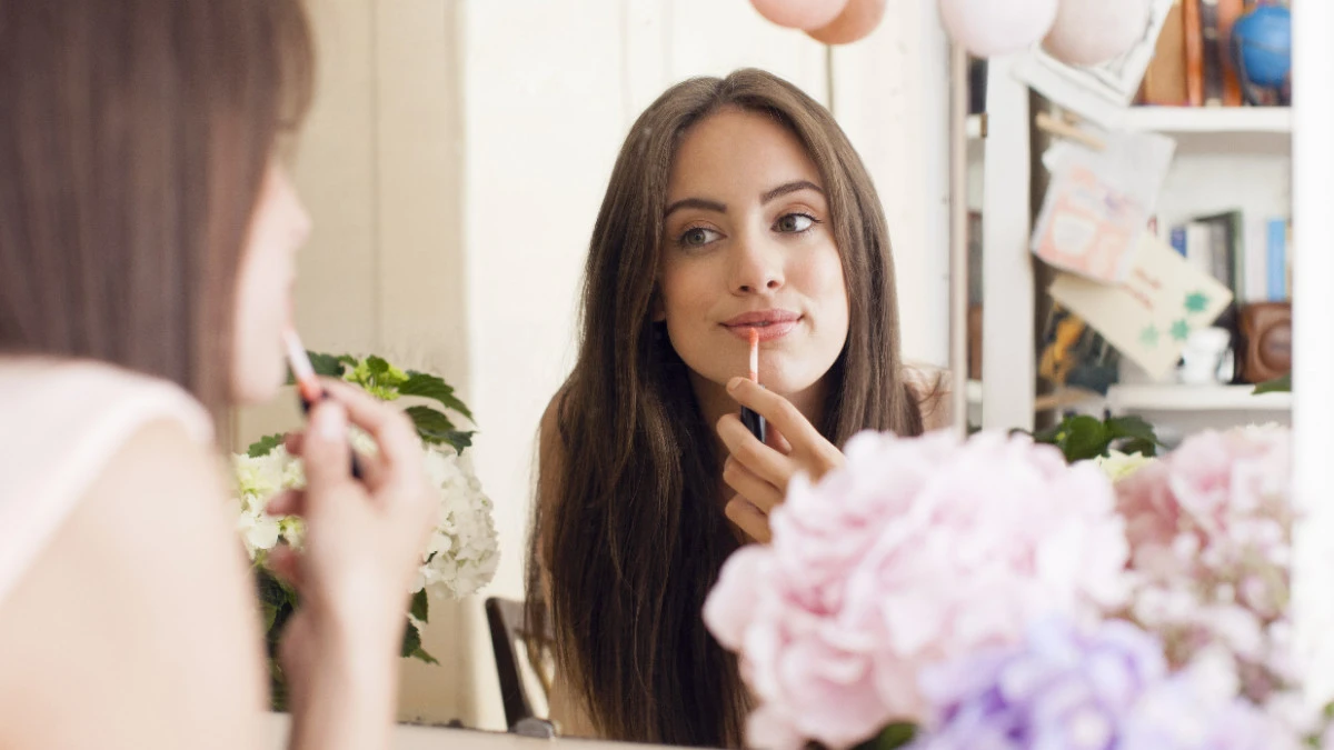  Frau trägt nude Lipgloss auf vor Spiegel 