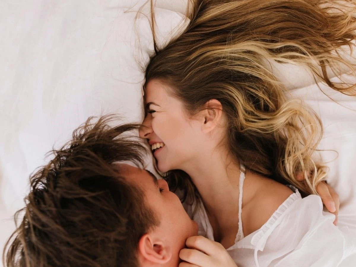  Lachende Frau liegt mit Mann auf Bett 