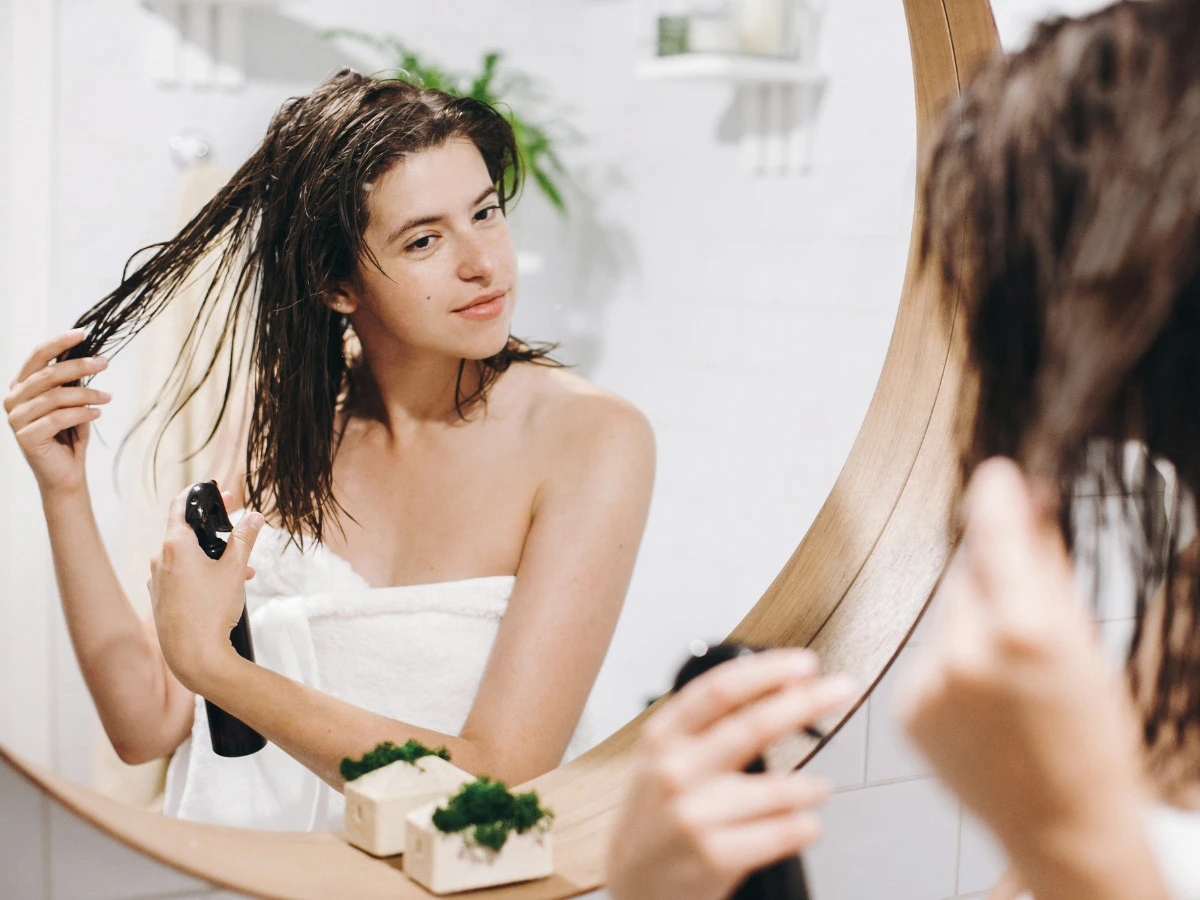  Frau trägt Hitzeschutz Spray in die nassen Haare auf vorm Spiegel im Badezimmer 