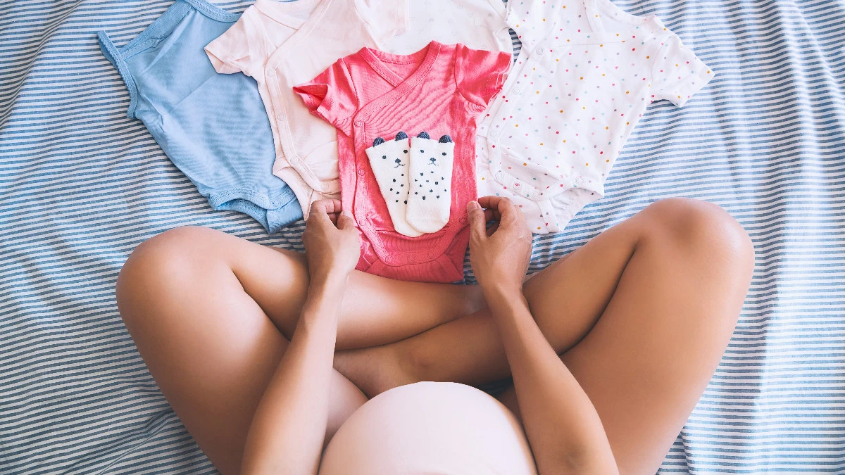  Frau mit Babybauch schaut sich Babykleidung an 