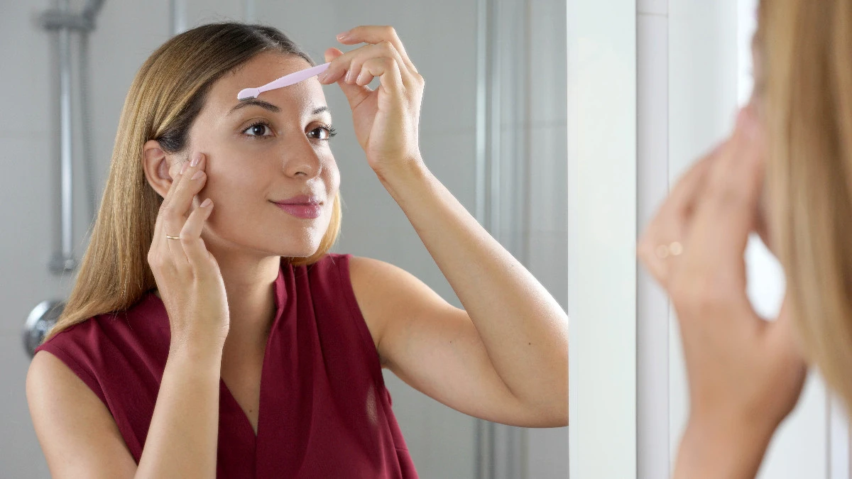  Frau trimmt sich die Augenbrauen mit Augenbrauentrimmer 