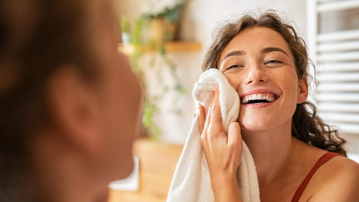  Frau trocknet sich Gesicht mit Handtuch ab nach Reinigung 